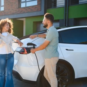 Happy couple charging their electric vehicle at their modern house, demonstrating commitment to eco friendly transportation